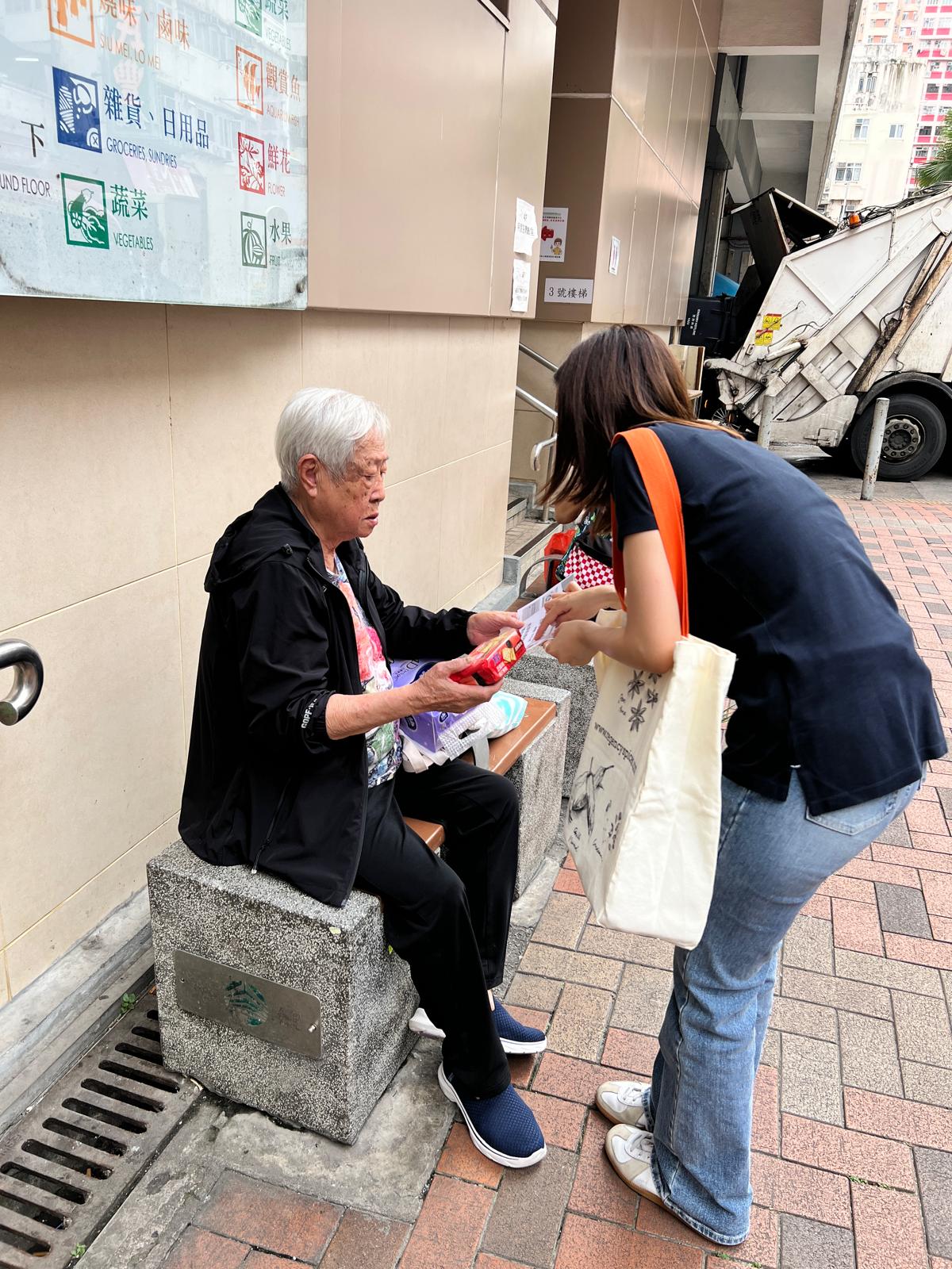 Volunteer handing a package to an elderly woman on a bench